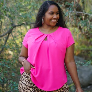 May include: A woman wearing a bright pink short-sleeved blouse with a keyhole neckline and leopard print shorts.