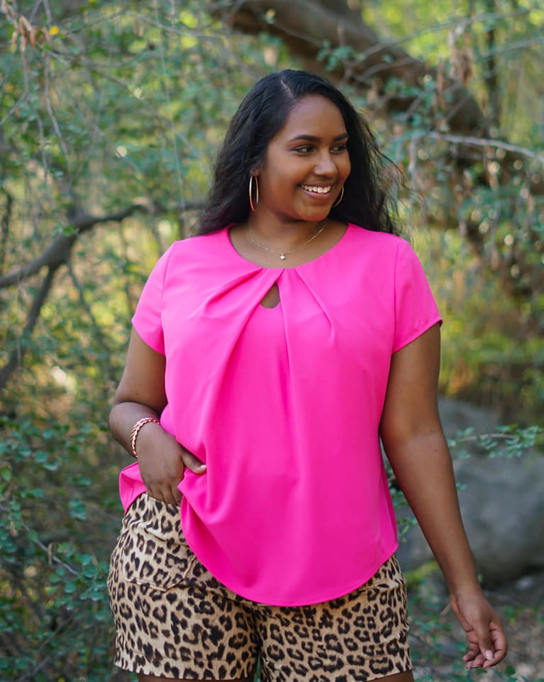 May include: A woman wearing a bright pink short-sleeved blouse with a keyhole neckline and leopard print shorts.
