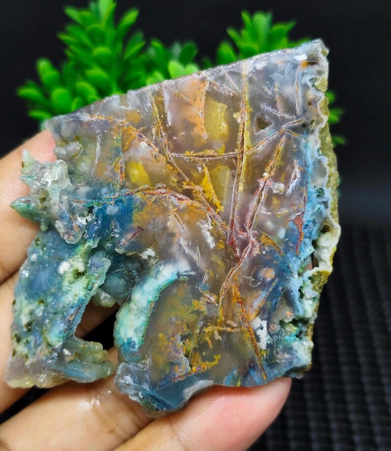 May include: A slice of agate with a variety of colors, including blue, green, yellow, and red. The agate has a natural, organic pattern and is translucent.