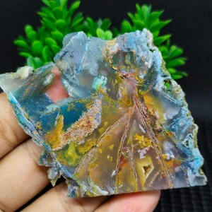 May include: A slice of agate with a variety of colors, including blue, green, yellow, and brown. The agate has a natural, rough texture and is translucent.