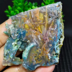 May include: A colorful agate slab with blue, green, yellow, and red patterns. The agate has a natural, rough edge and is translucent.