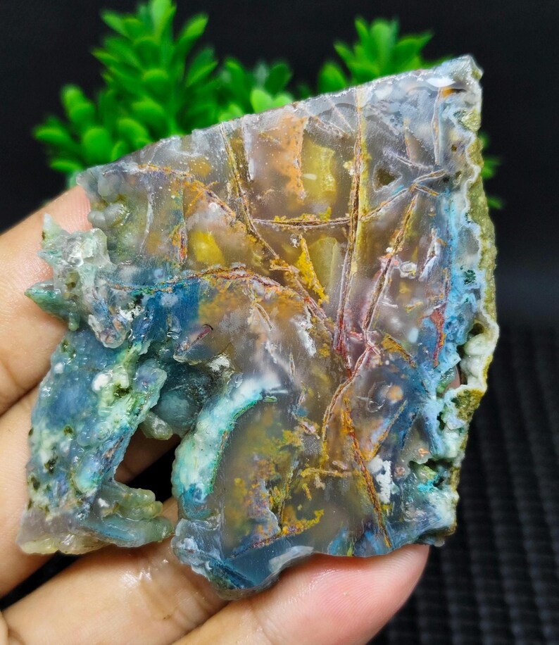 May include: A colorful agate slab with blue, green, yellow, and red patterns. The agate has a natural, rough edge and is translucent.