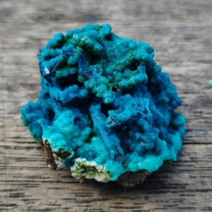 Peut inclure: Spécimen minéral naturel vibrant, présentant une combinaison saisissante de teintes turquoise et bleu sarcelle. La structure cristalline a un aspect texturé et poreux, avec des zones bleu foncé et des touches de vert. La base est un mélange de brun et de blanc.