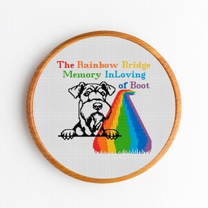May include: A cross-stitch embroidery hoop with a black and white illustration of a dog looking over a rainbow with the text "The Rainbow Bridge Memory In Loving of Boot".