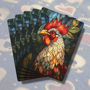 May include: A stack of playing cards featuring a colorful stained glass rooster design. The rooster is depicted in a jungle setting with green and brown leaves.