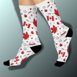 May include: White socks with a repeating pattern of red maple leaves, Canadian flags, hearts, acorns, and squirrel illustrations. The socks have black heels and toes, and the word "CANADA" is printed on the top of the socks.