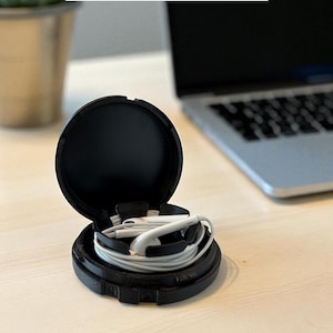 Könnte beinhalten: Schwarze, runde Universalhülle, geöffnet, um weiße Ohrhörer mit weißem Kabel zu zeigen. Die Hülle befindet sich auf einer hellen Holzoberfläche. Der Text "Universal Case" steht oben im Bild.