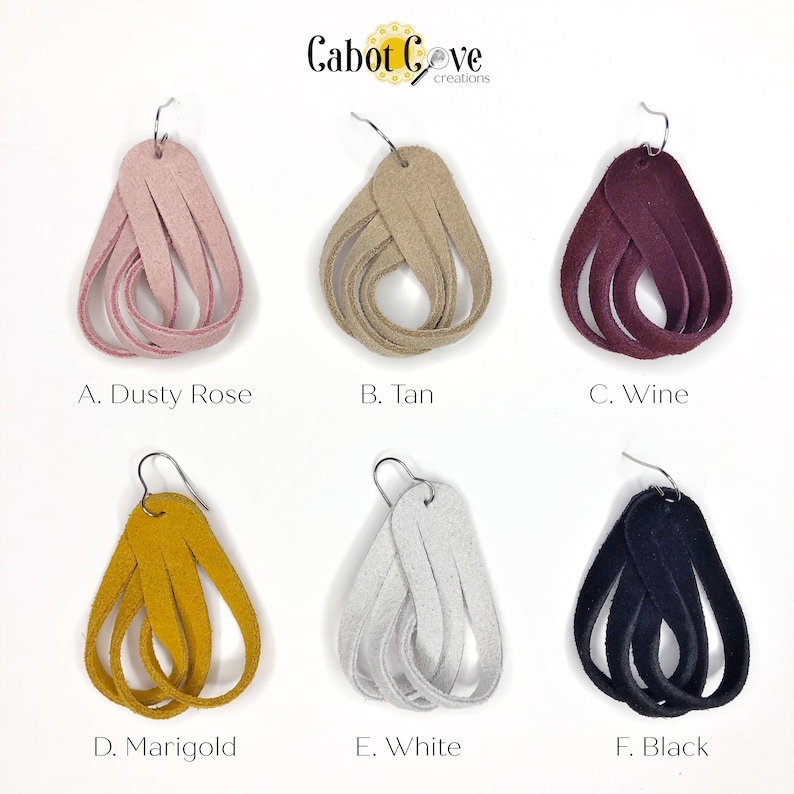 May include: Six pairs of suede leather earrings in various colors, including dusty rose, tan, wine, marigold, white, and black. The earrings are all in the shape of a teardrop and have a knotted design. Cabot Cove creations.