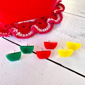 May include: Four pairs of colorful half-circle earrings. The earrings are red, yellow, green, and blue. The earrings are on a white surface.