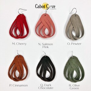 May include: Six pairs of leather earrings in various colors, including cherry red, salmon pink, pewter, cinnamon, dark chocolate, and olive green. The earrings are all in the shape of a teardrop and are made of braided leather. The earrings are labeled with letters and color names.