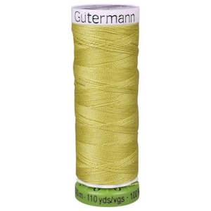 May include: A spool of Gutermann thread in a light olive green color. The spool has a white top with the brand name and a green base with text indicating the length of the thread. The thread is tightly wound around the spool.