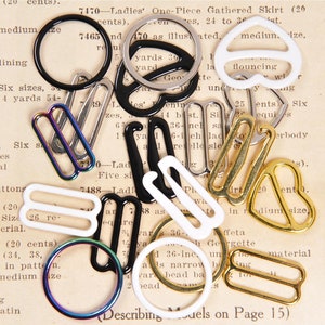 May include: Assortment of metal bra strap adjusters in various shapes and sizes. The adjusters are in gold, silver, black, and white.