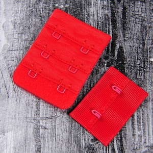 May include: Two red bra strap extenders with metal hooks. The extenders are made of a soft, stretchy fabric.