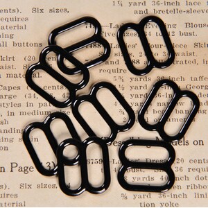 May include: A close-up of ten black metal D-rings, scattered on a page of text. The D-rings are approximately 1 inch in diameter.