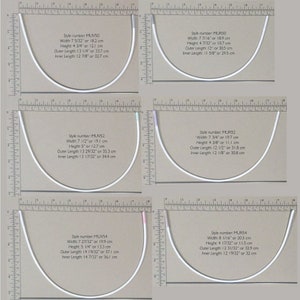 May include: Four different sizes of white metal bra strap rings, measured in inches and centimeters. The rings are displayed on a brown surface with a ruler.