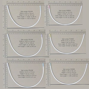 May include: Four different styles of white plastic bra strap adjusters, each with a different length and width. The adjusters are measured in inches and centimeters. The adjusters are displayed on a white background with a ruler.