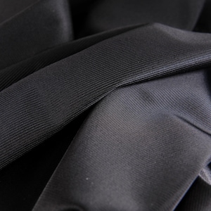 May include: Close-up of black fabric with a textured, ribbed surface. The fabric is folded and draped, showing the texture and drape of the material.