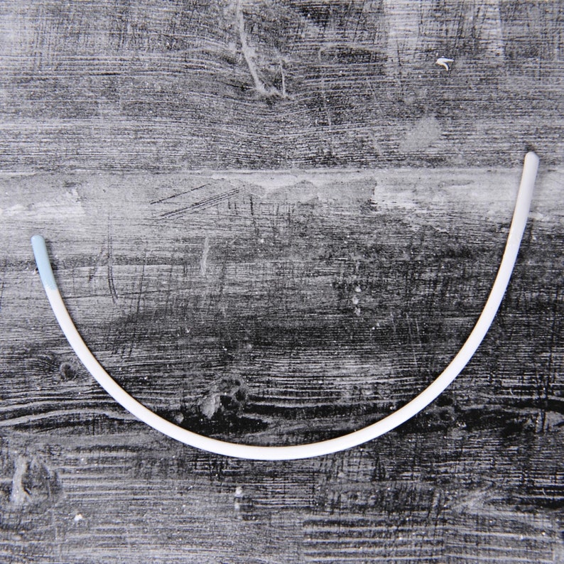 May include: A white plastic underwire bra strap with a light blue end cap.
