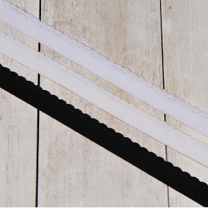 May include: Two white elastic bands with scalloped edges and one black elastic band with scalloped edges. The bands are lying on a light wood surface.