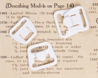 May include: Four white plastic bra strap adjusters. The adjusters are square with a rectangular opening in the center. The text "Describing Models on Page 14" is visible in the background.