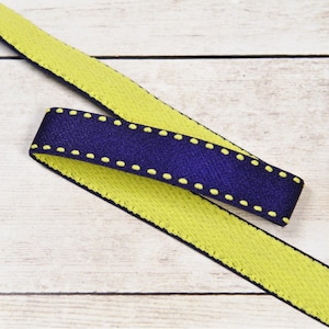 May include: A yellow and dark blue ribbon with a dotted stitch detail. The ribbon is woven and has a textured surface.