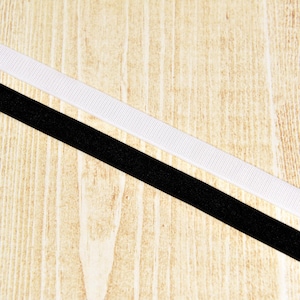 May include: A close-up of two strips of fabric, one white and one black, lying on a wooden surface. The white strip is on top of the black strip.