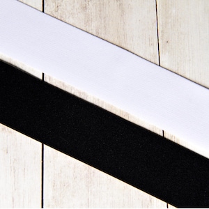 May include: A white and black fabric ribbon with a diagonal pattern. The ribbon is on a light wood background.