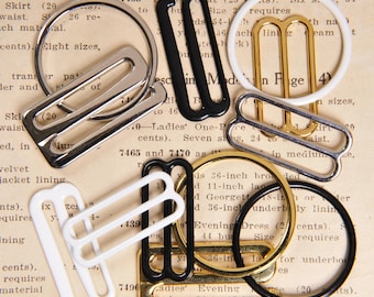 May include: Assortment of metal bra strap sliders in various sizes and colors, including silver, gold, black, and white. The sliders are arranged on a printed page with text about bra sizes and materials.