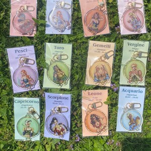 Puede incluir: Doce llaveros coloridos con signos del zodíaco y fechas. Cada llavero tiene un anillo de metal dorado y un dije redondo de plástico transparente con una ilustración colorida de un signo del zodíaco y sus fechas correspondientes.