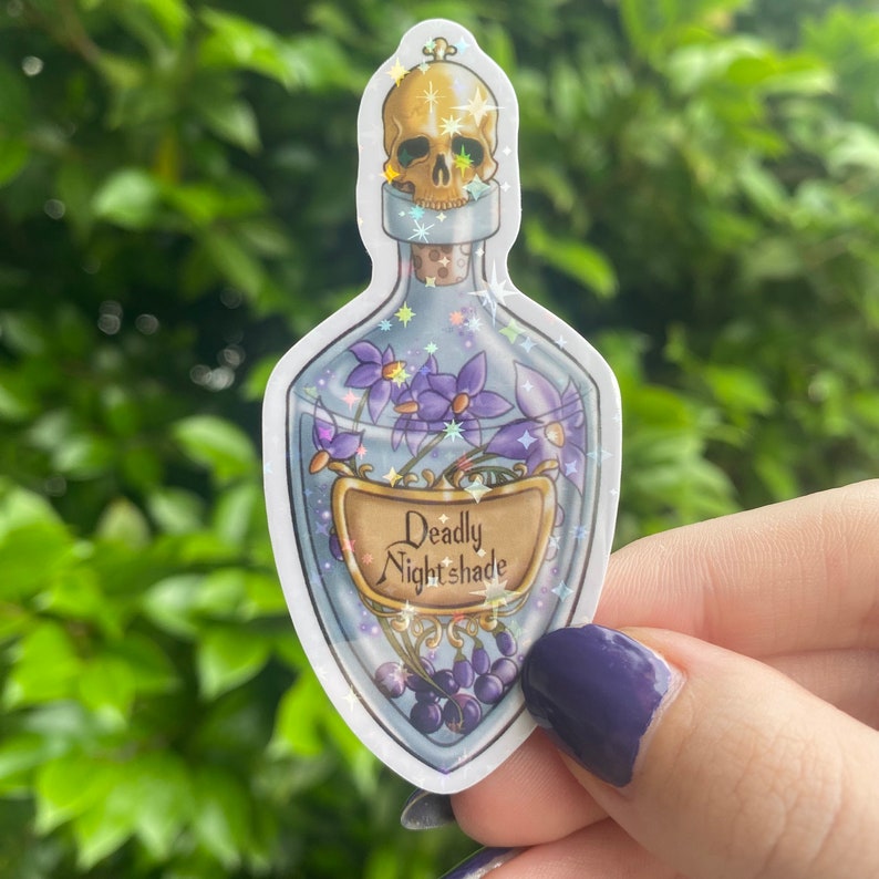 Puede incluir: Una botella de vidrio azul con un tap&oacute;n de calavera y flores moradas en su interior. La botella tiene una etiqueta que dice "Deadly Nightshade".