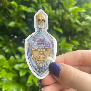 Puede incluir: Una botella de vidrio transparente con un tap&oacute;n de calavera y una etiqueta que dice "Deadly Nightshade". La botella est&aacute; llena de flores moradas y bayas negras. La botella est&aacute; rodeada de un fondo brillante y brillante.