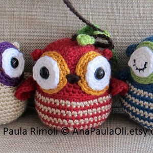 May include: Three crocheted owl ornaments with different colored bodies and eyes. The owls are beige, red, and blue with green, purple, and yellow accents. The owls have white eyes with black pupils and are all winking.
