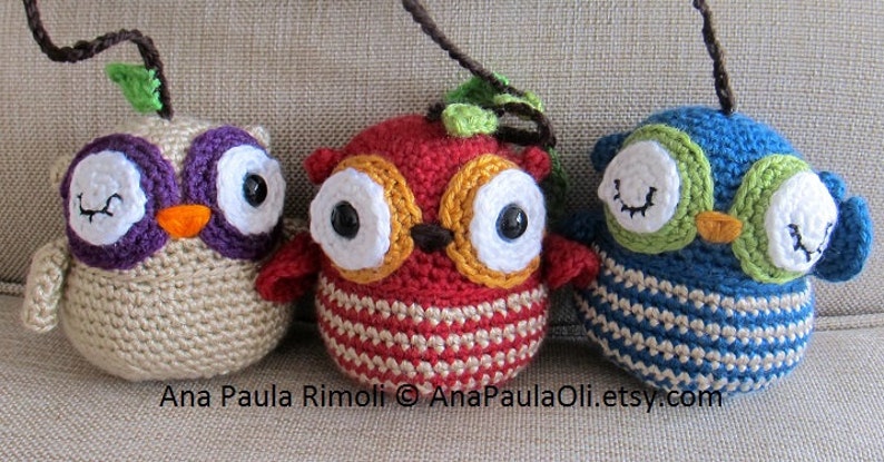 May include: Three crocheted owl ornaments with different colored bodies and eyes. The owls are beige, red, and blue with green, purple, and yellow accents. The owls have white eyes with black pupils and are all winking.