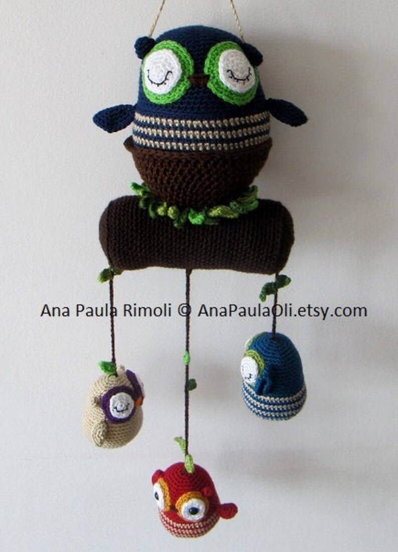 May include: A crocheted owl mobile with a brown log base and four hanging owls. The owls are crocheted in various colors, including blue, green, red, and beige. The mobile is suspended from the ceiling with a string.