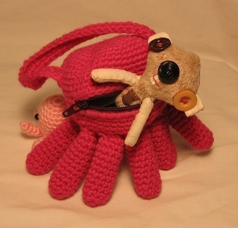 Puede incluir: Un pulpo de crochet rosa con una bolsa con cremallera. Un peque&ntilde;o pulpo de crochet rosa y un juguete de peluche beige con ojos negros y una nariz de bot&oacute;n amarillo est&aacute;n dentro de la bolsa.
