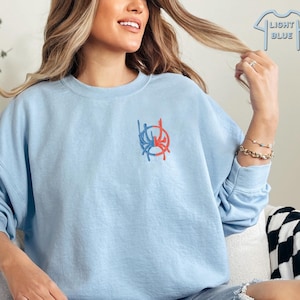 May include: A light blue sweatshirt with a red and blue graphic design on the front. The graphic is a stylised circle with a dripping effect.