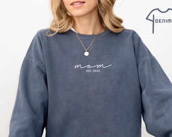 May include: A blue sweatshirt with the word "mom" written in white script with the text "EST. 2024" underneath.