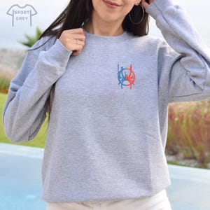 May include: A grey sweatshirt with a red and blue graphic design on the front. The design is a circle with a stylised flame inside.