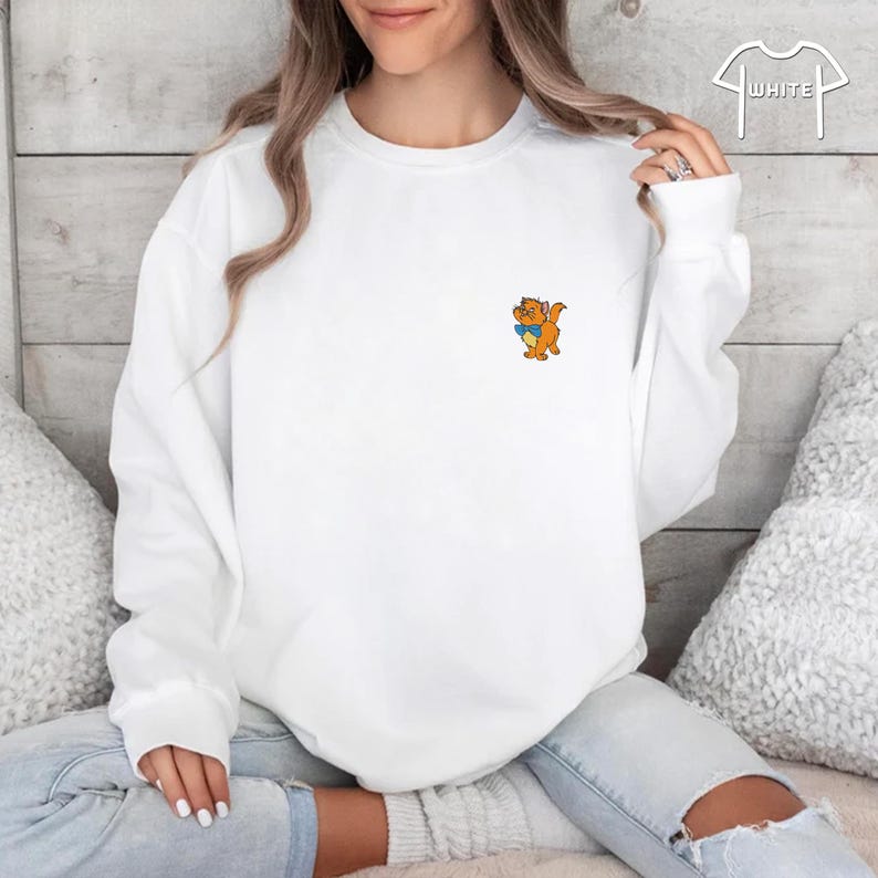 May include: White sweatshirt featuring a small cartoon graphic of an orange cat holding a blue book. The sweatshirt has a crew neck and long sleeves. The word "WHITE" is printed on the upper right corner.