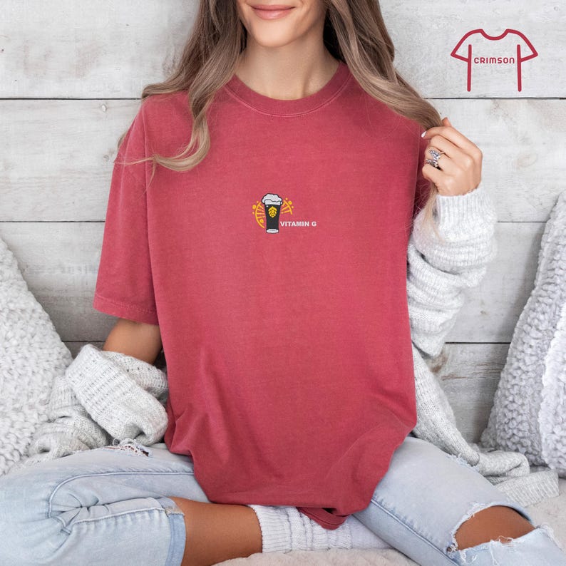 May include: A red t-shirt with a small graphic of a beer glass with foam and the words "Vitamin G". The shirt is a solid color and has short sleeves.