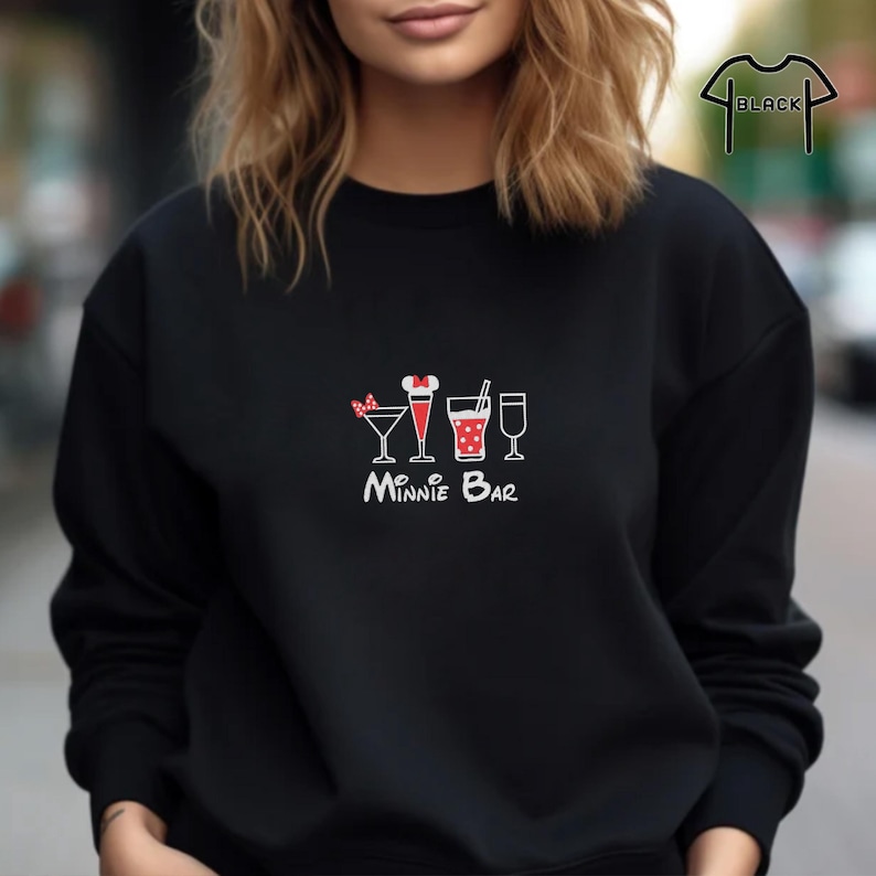 Puede incluir: Sudadera negra con un gr&aacute;fico blanco de una fila de cinco vasos de c&oacute;ctel con un lazo rojo en el primer vaso y el texto "Minnie Bar" debajo.