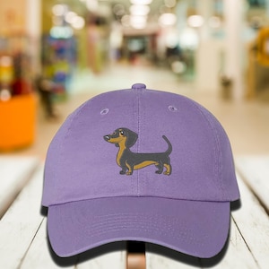 May include: Purple baseball cap with a cartoon dachshund embroidered on the front.