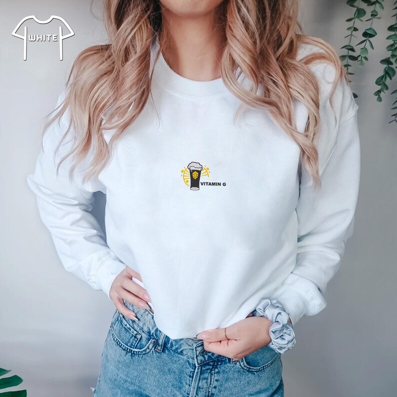Peut inclure: Sweat-shirt blanc &agrave; col rond et manches longues. Il pr&eacute;sente un petit motif d'un verre noir avec un design jaune et le texte "VITAMIN G". Le sweat-shirt est fait d'une mati&egrave;re douce.