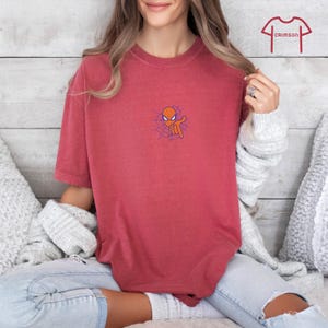 May include: A red t-shirt with a cartoon image of Spider-Man's head with a web behind it.