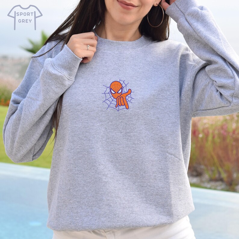 May include: A gray sweatshirt with a small orange and blue embroidered image of Spiderman on a web. The text "SPORT GREY" is visible in the top left corner of the image.