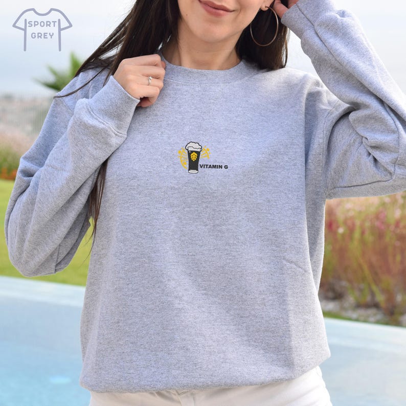 Peut inclure: Sweat-shirt gris sport avec un petit dessin d'un verre &agrave; bi&egrave;re avec de la mousse et le texte "VITAMIN G" en noir. Le sweat-shirt est de couleur gris clair.
