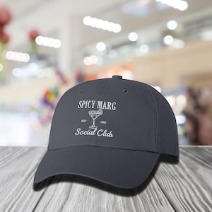 May include: A dark blue baseball cap with the text "Spicy Marg Social Club Est. 1983" and a white illustration of a margarita glass with a lime wedge.