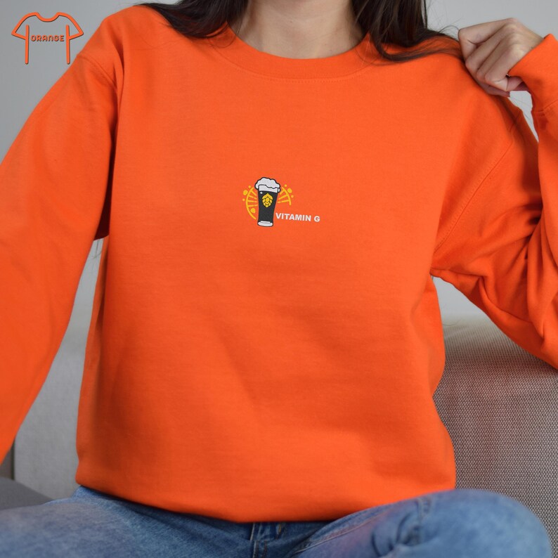 Peut inclure: Sweat-shirt orange vif avec un petit motif de verre &agrave; bi&egrave;re avec de la mousse et le texte "VITAMIN G". Le haut &agrave; col ras du cou et &agrave; manches longues est en mati&egrave;re souple.