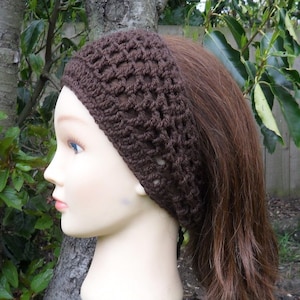 May include: A brown crocheted headband with a lacy pattern. The headband is worn on a mannequin with long brown hair.