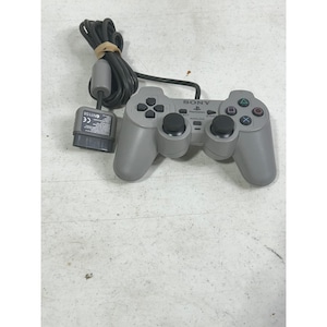 May include: A gray PlayStation 2 controller with a black cord and connector. The controller has the Sony logo and the word "ANALOG" printed on it. The controller has a directional pad, four action buttons, and two analog sticks.
